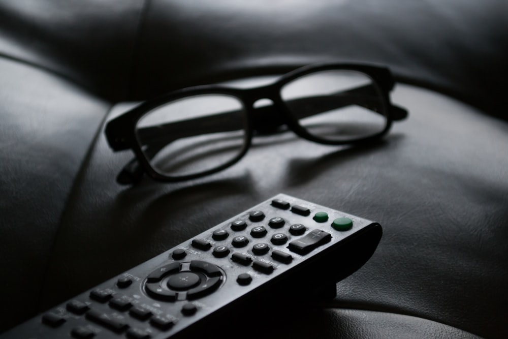 grayscale photo of remote beside eyeglasses