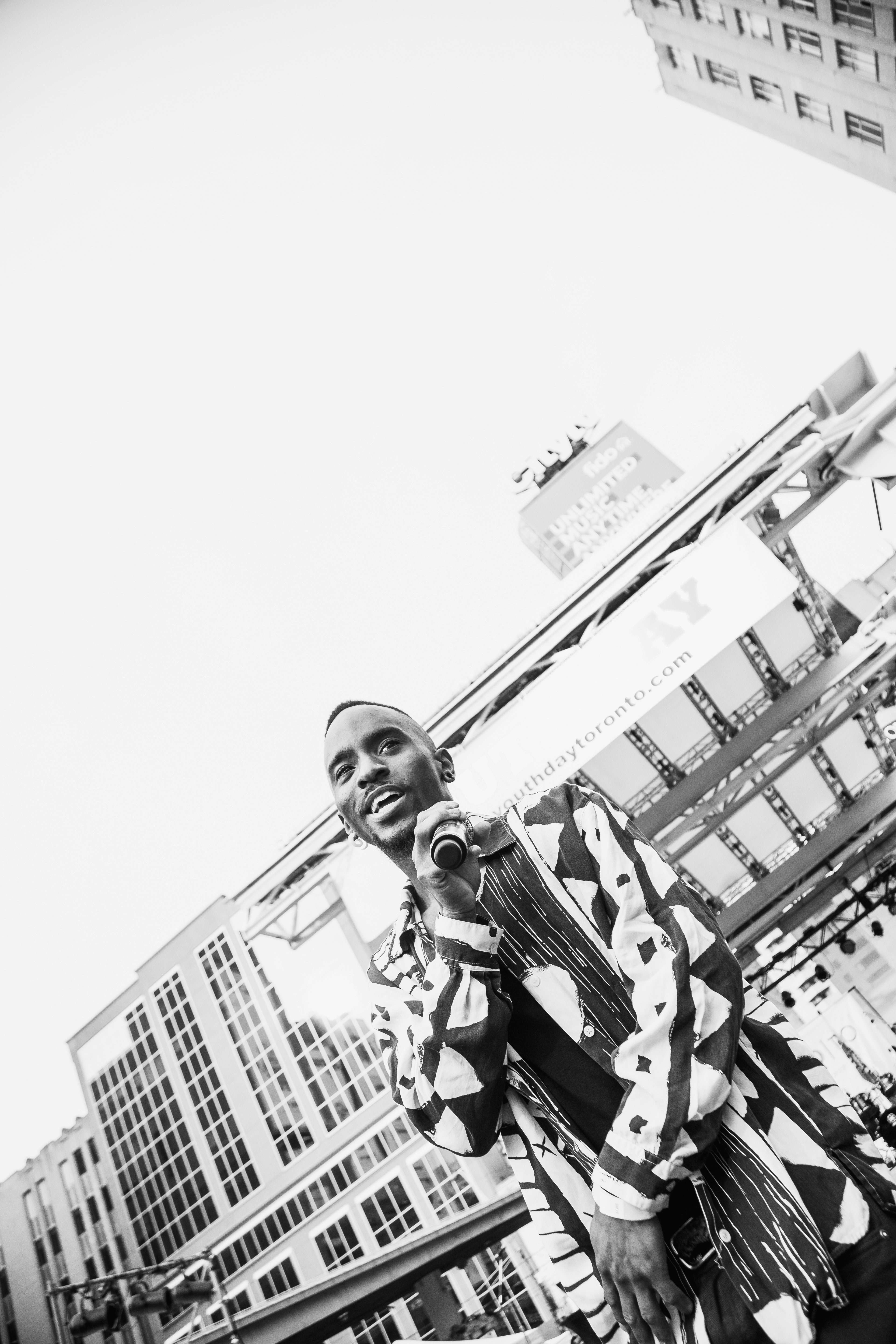 man holding microphone while standing outdoor grayscale photography