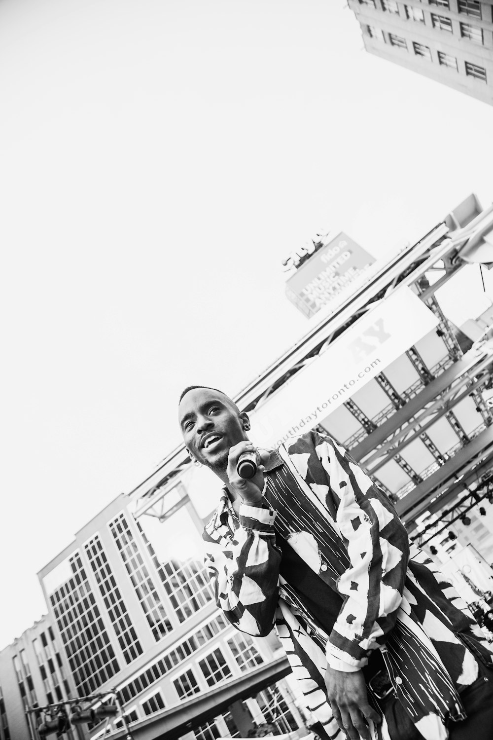 man holding microphone while standing outdoor grayscale photography