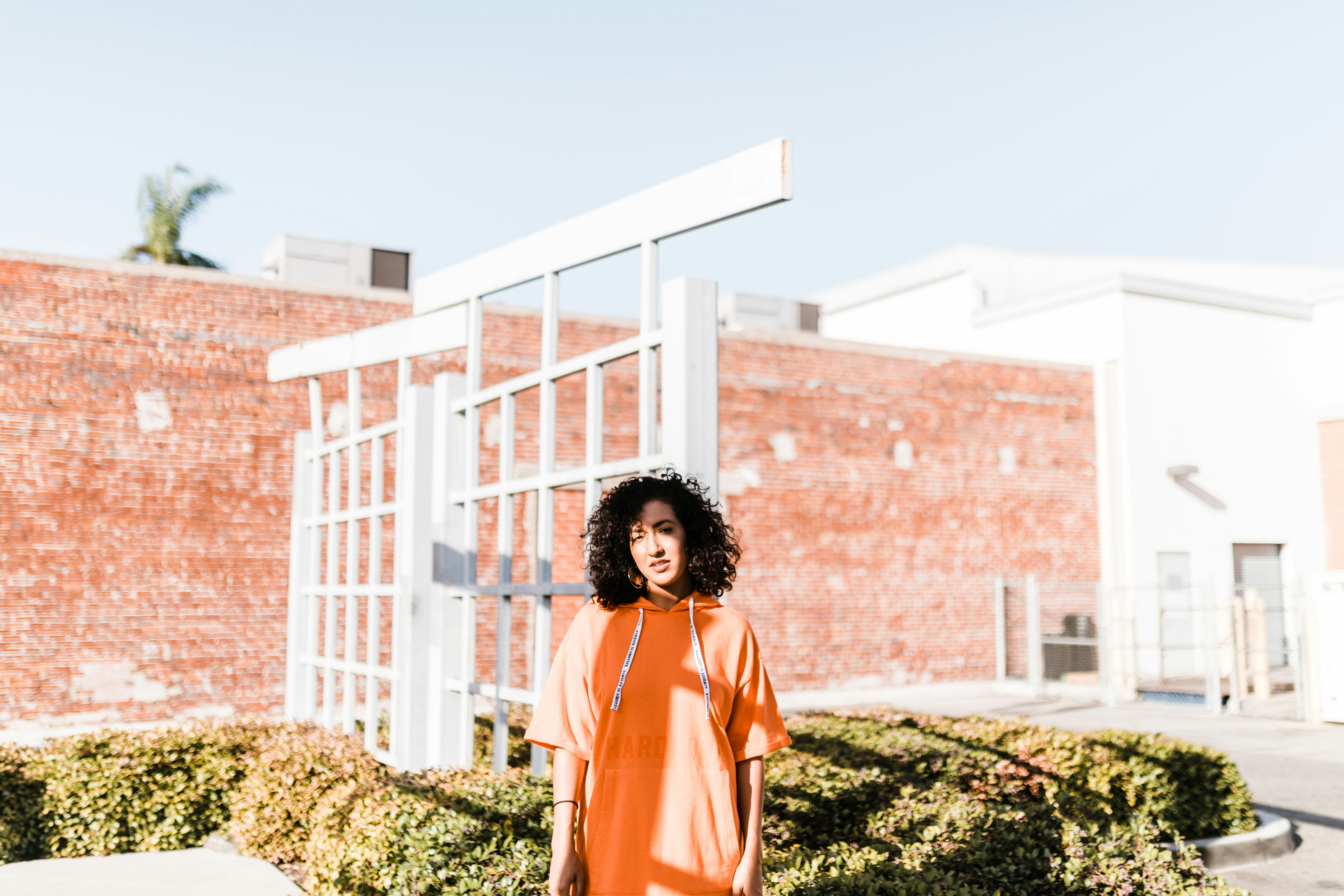 woman in orange pullover hoodie standing near white gate during daytime