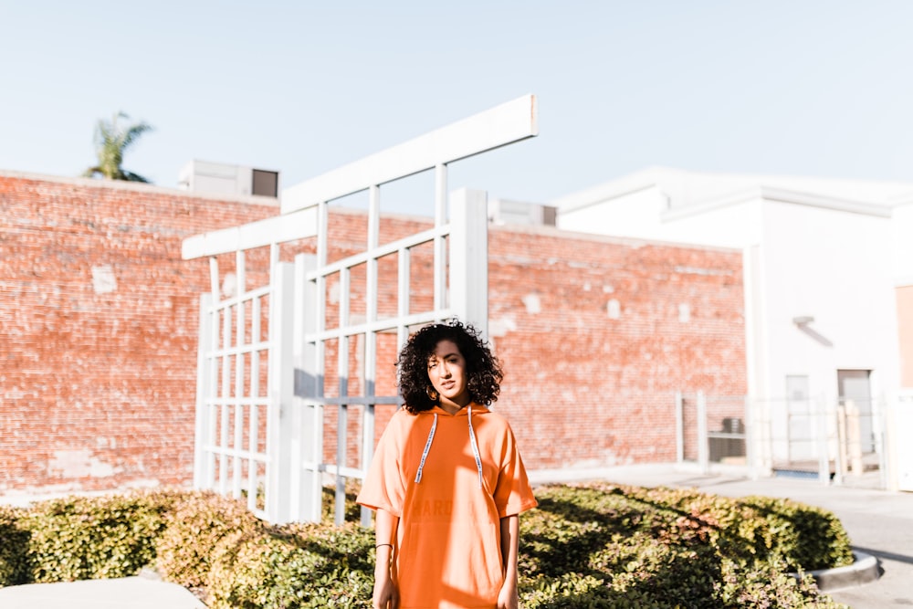 woman in orange pullover hoodie standing near white gate during daytime