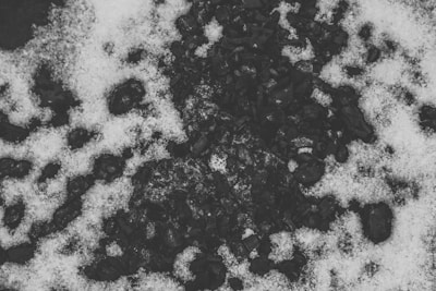 Black coal rocks are scattered on the ground, partially covered by patches of white snow. The scene creates a strong contrast between the dark and light areas, emphasizing the rough texture of the coal and the soft, powdery appearance of the snow.