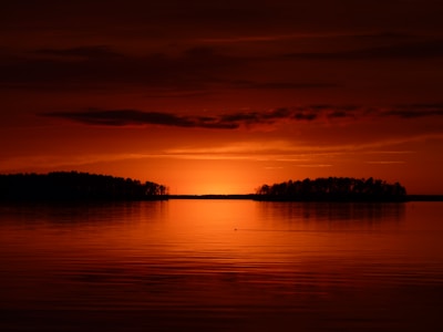 Sunset over a calm lake, reflected perfectly in the water with an island at center.