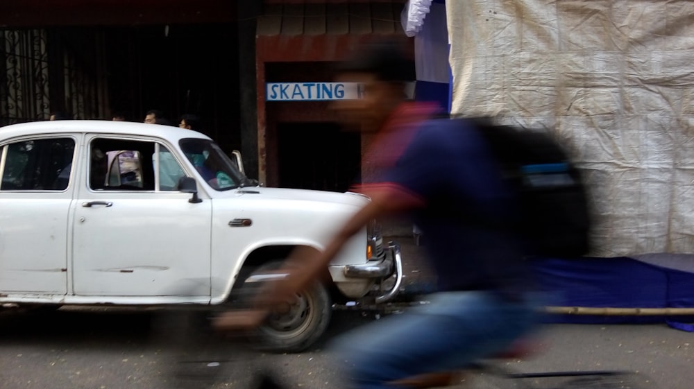 man riding bicycle beside white car