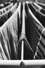 Clothes hang on a drying rack with thin metal rods, featuring a mixture of light and dark fabrics. The perspective is up close, emphasizing the texture and pattern of the clothing. The image is in black and white, creating a classic and timeless feel.