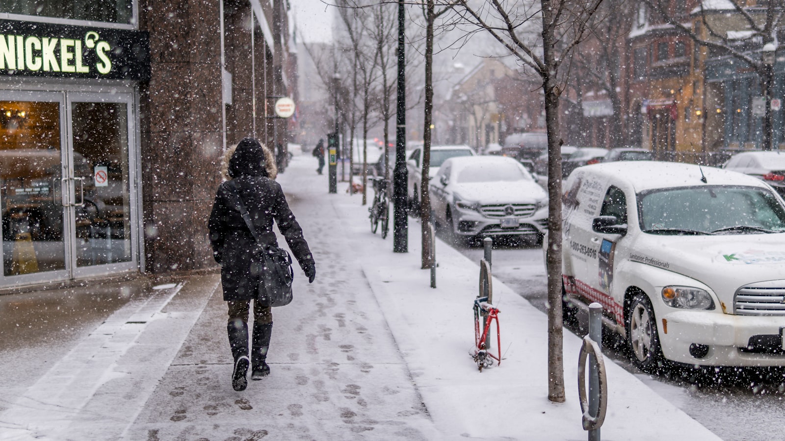 Pedestrian walking on a snowy Toronto sidewalk during active snowfall, a winter survival scene for Canadian students