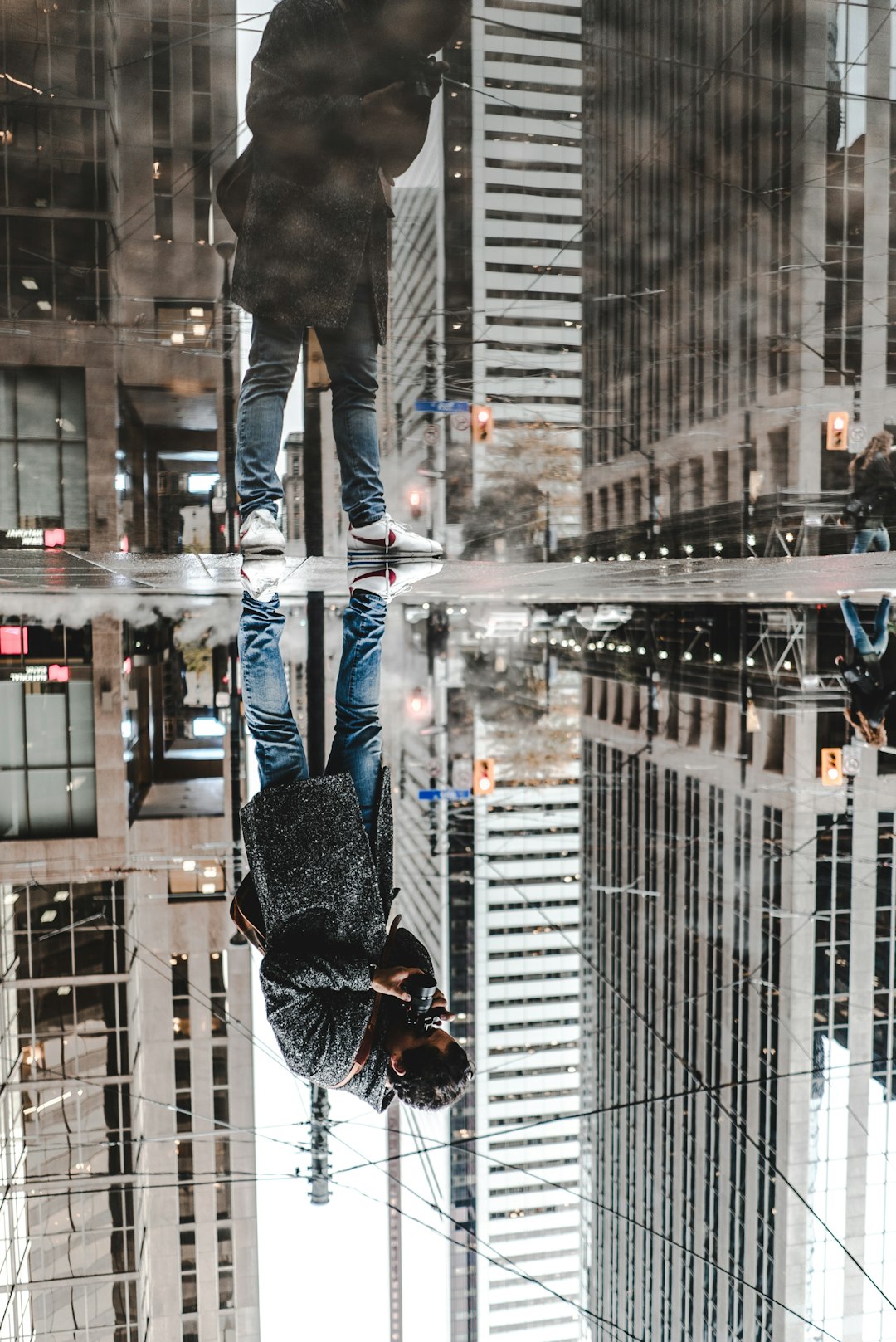 water mirror reflection photography of man standing on pavement front of buildings