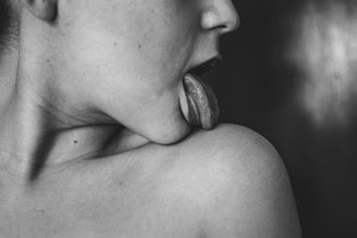 grayscale photo of woman licking her shoulder
