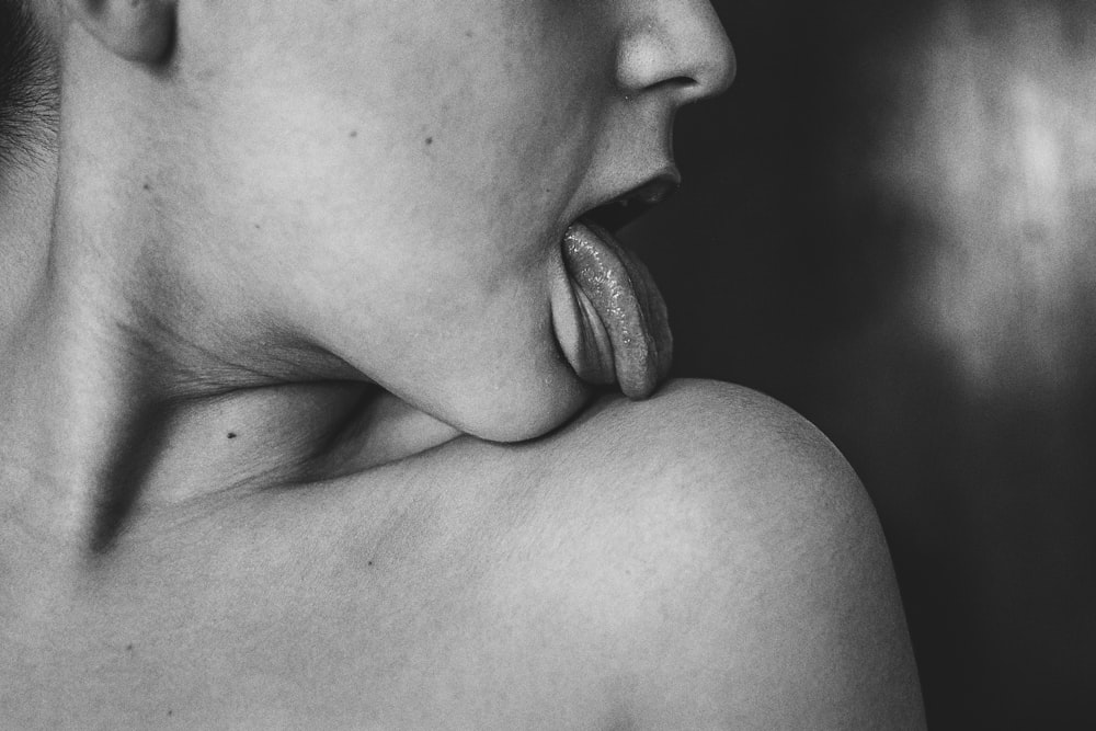 grayscale photo of woman licking her shoulder