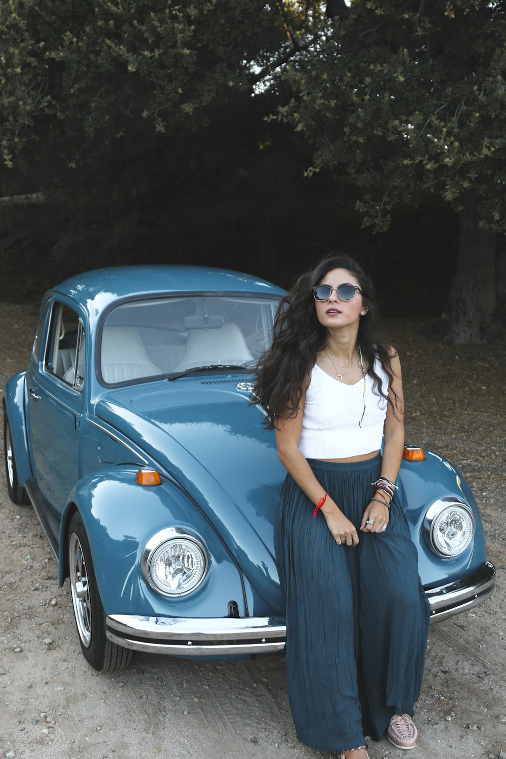 woman in white tank top and black skirt leaning on blue volkswagen beetle