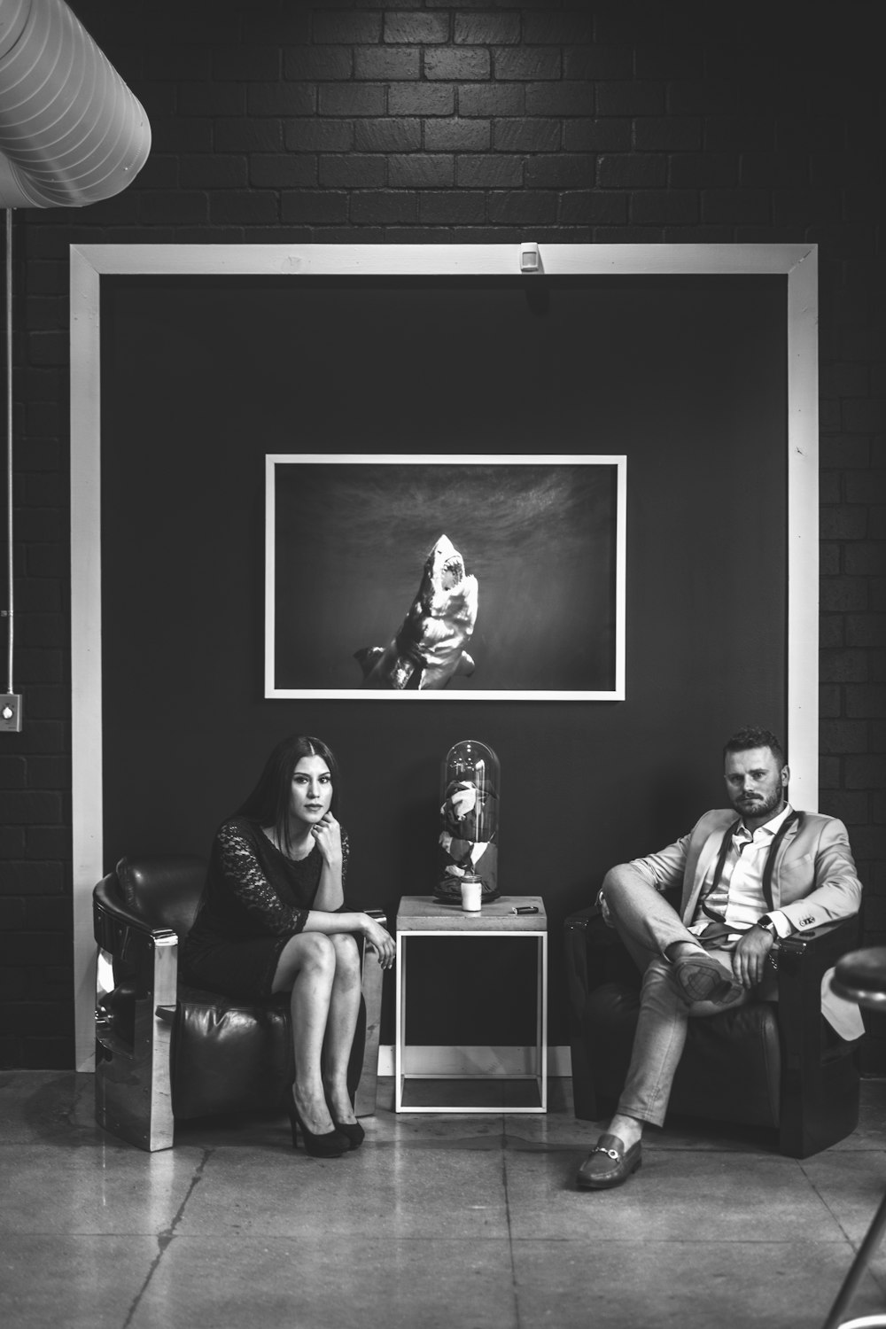 grayscale photo of man and woman sitting on sofa chairs
