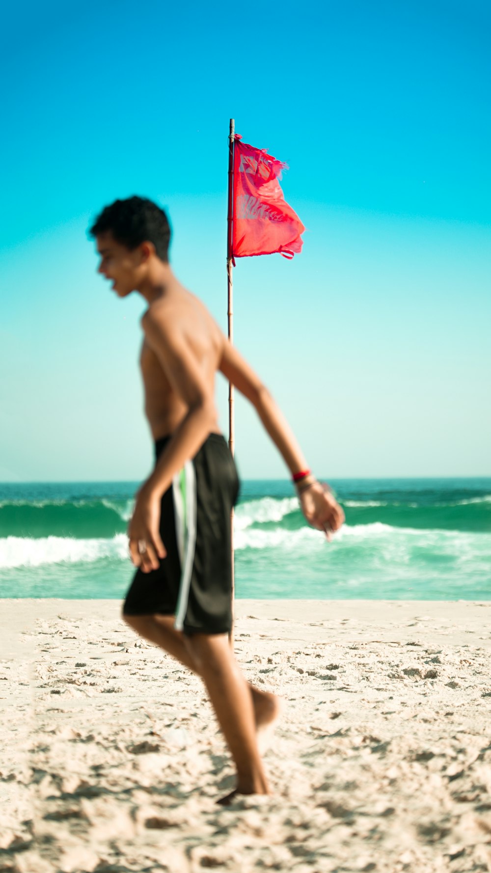 selective focus photo of red flag on brown pole near body of water
