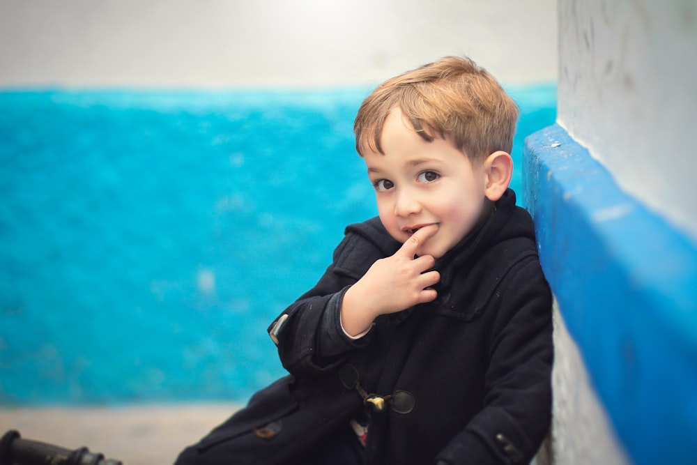 boy in black jacket sitting on blue plastic chair