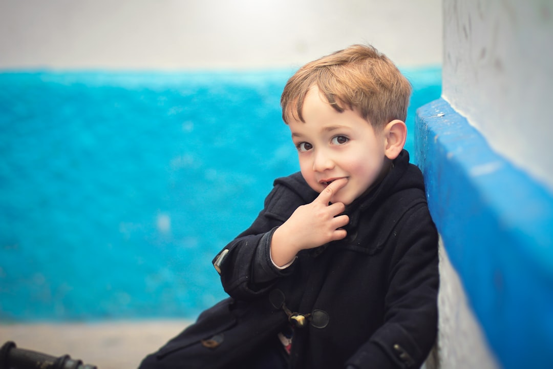 boy in black jacket sitting on blue plastic chair