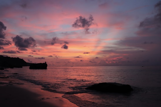 Sunset view over Cala Rossa beach with vibrant orange and pink skies reflecting on the calm sea.