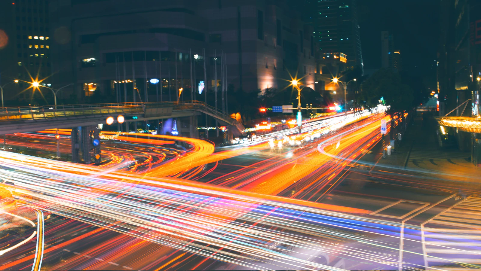 A long exposure of traffic on a multi-lane road running past concrete buildings