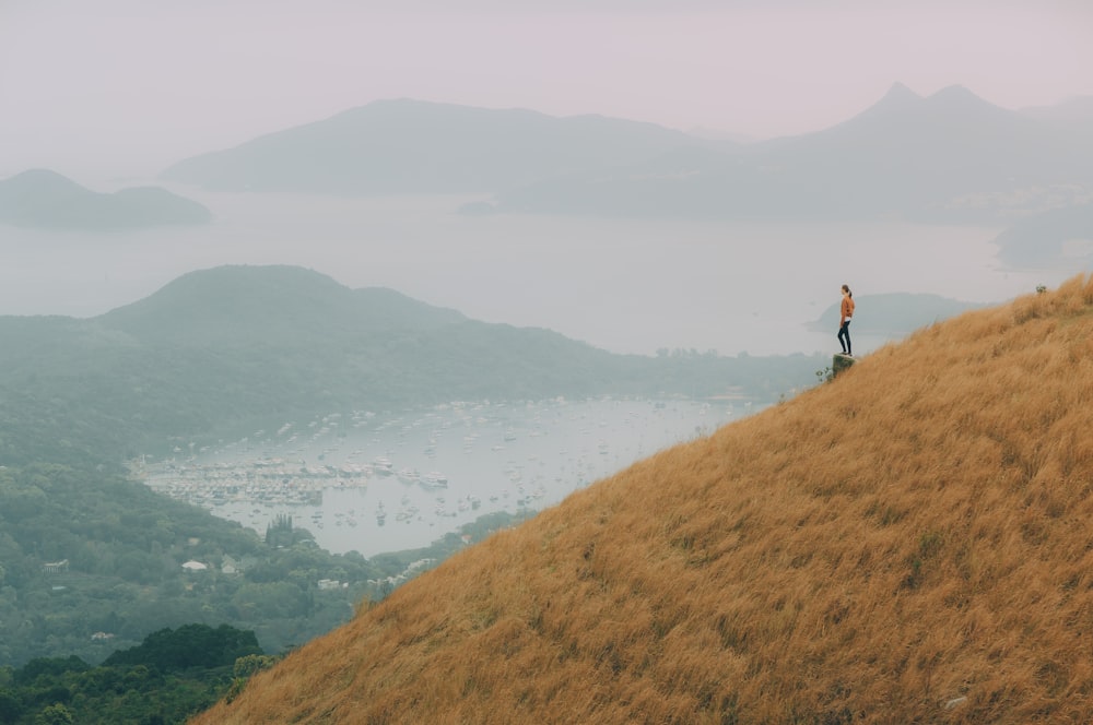 woman standing on top of stone facing village near body of water and mountain at distance