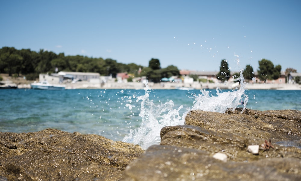 impact of wave on brown rock with view of houses at distance