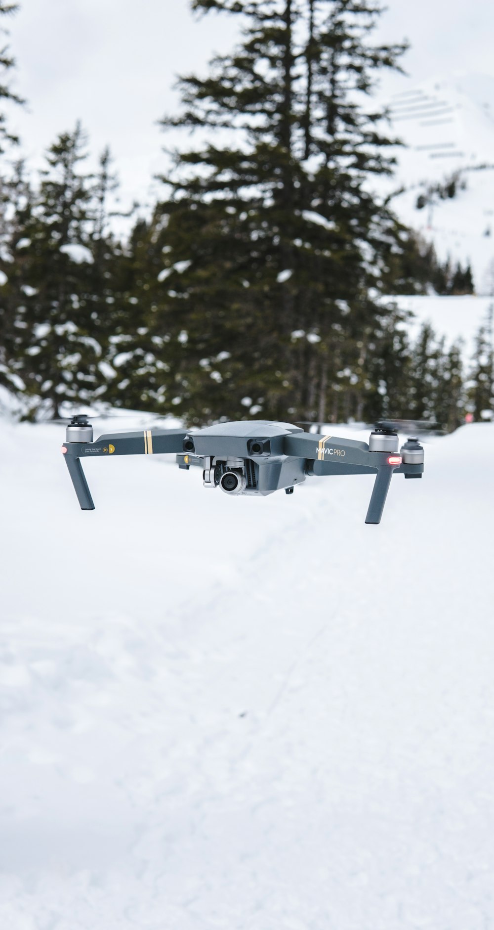 grauer fliegender Quadrocopter in der Nähe von Bäumen mit Schnee