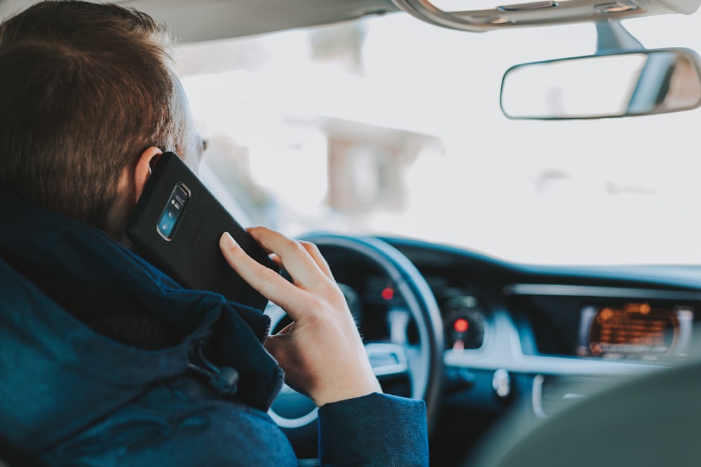 Mann sitzt auf Autositz vorne am Lenkrad und hält Telefon in der Hand