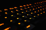 Close-up of a sleek gaming keyboard with orange neon backlighting on a dark desk.