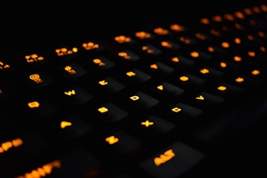Close-up of a sleek mechanical keyboard with orange neon backlighting on a dark desk