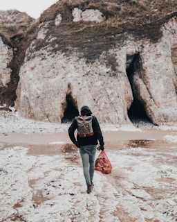 person black shirt with backpack walking on seashore