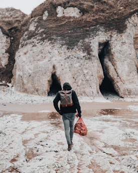 person black shirt with backpack walking on seashore