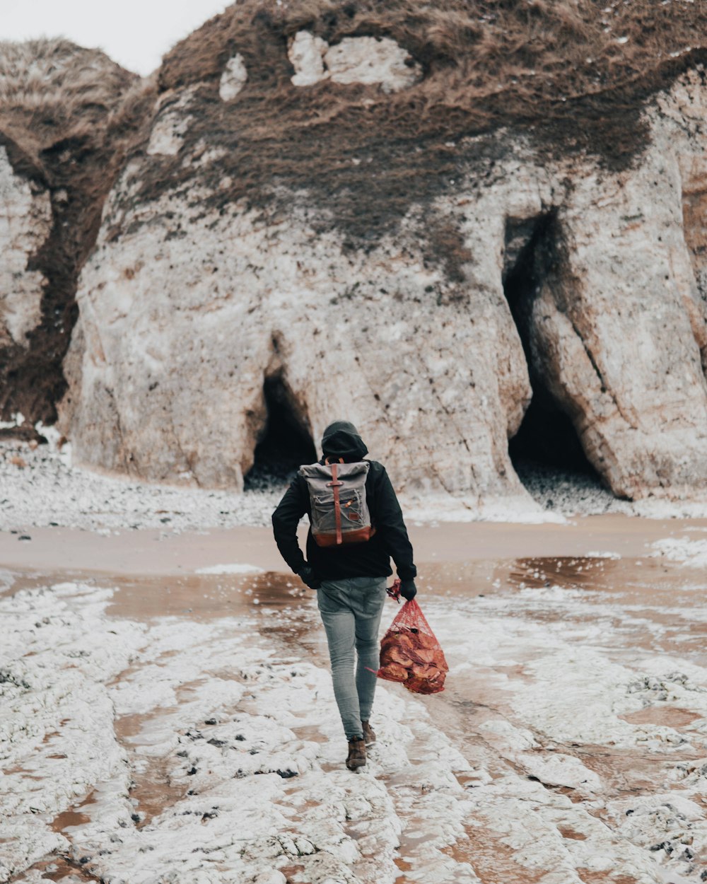 person black shirt with backpack walking on seashore