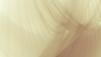 Delicate, flowing layers of soft fabric create a sense of gentle movement and texture. The material appears to be translucent, allowing light to pass through in a diffused manner.