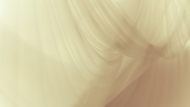 Delicate, flowing layers of soft fabric create a sense of gentle movement and texture. The material appears to be translucent, allowing light to pass through in a diffused manner.