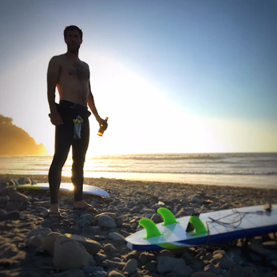 Lifestyle shot of a surfer with a summer vibe t-shirt on a beach at sunset.