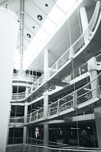 A multi-level modern interior with curved balconies and railings. The architecture features a striking combination of straight lines and rounded elements. The ceiling has large windows that allow natural light to brighten the space.