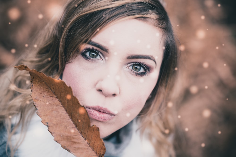 selective focus photo of woman holding brown leaf