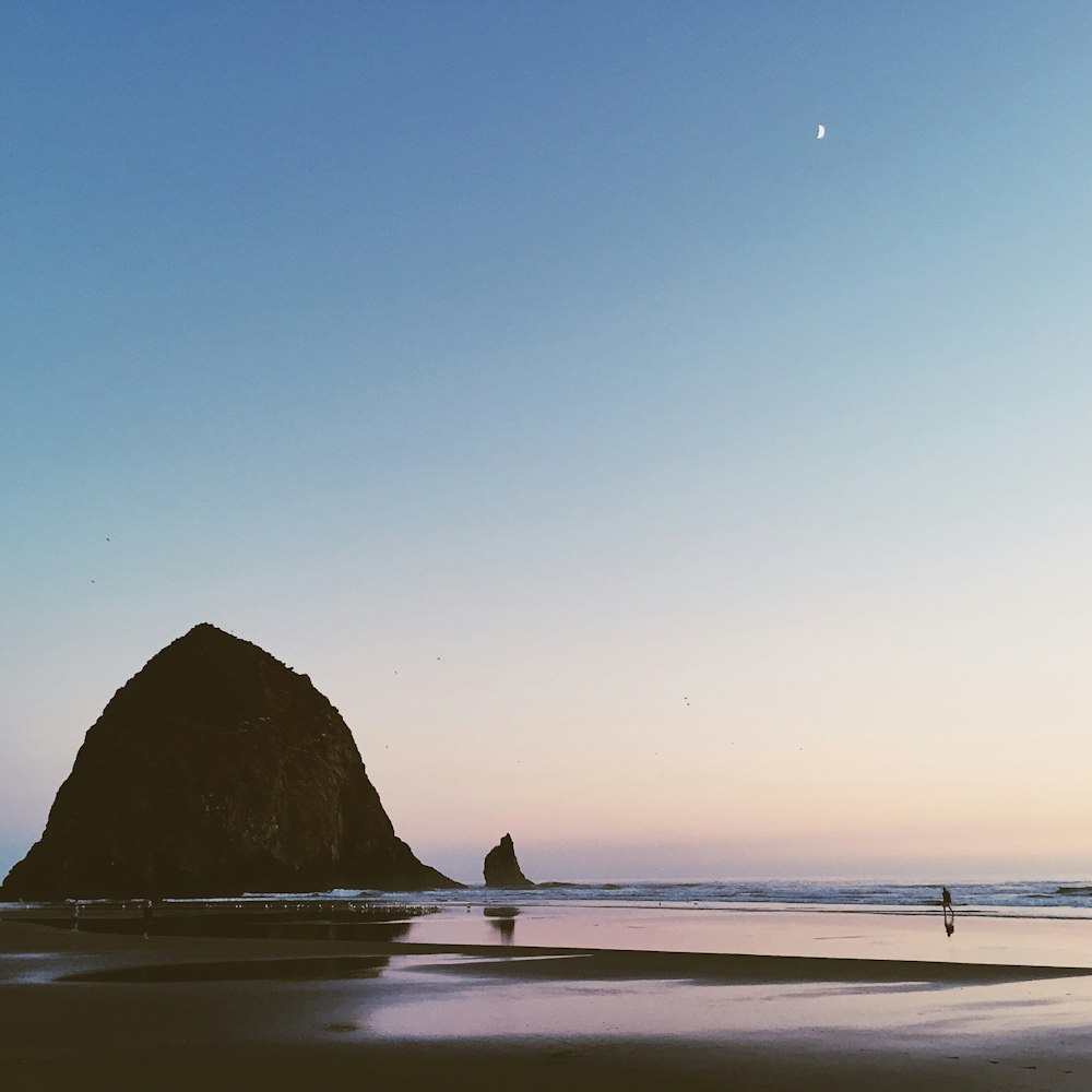 photo of person on seashore far away from islet