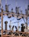 A series of industrial electrical insulators and transformers positioned on a grid-like metal structure. The arrangement is orderly, with cylindrical and spiral shapes dominating the composition. The sky in the background is clear and blue.