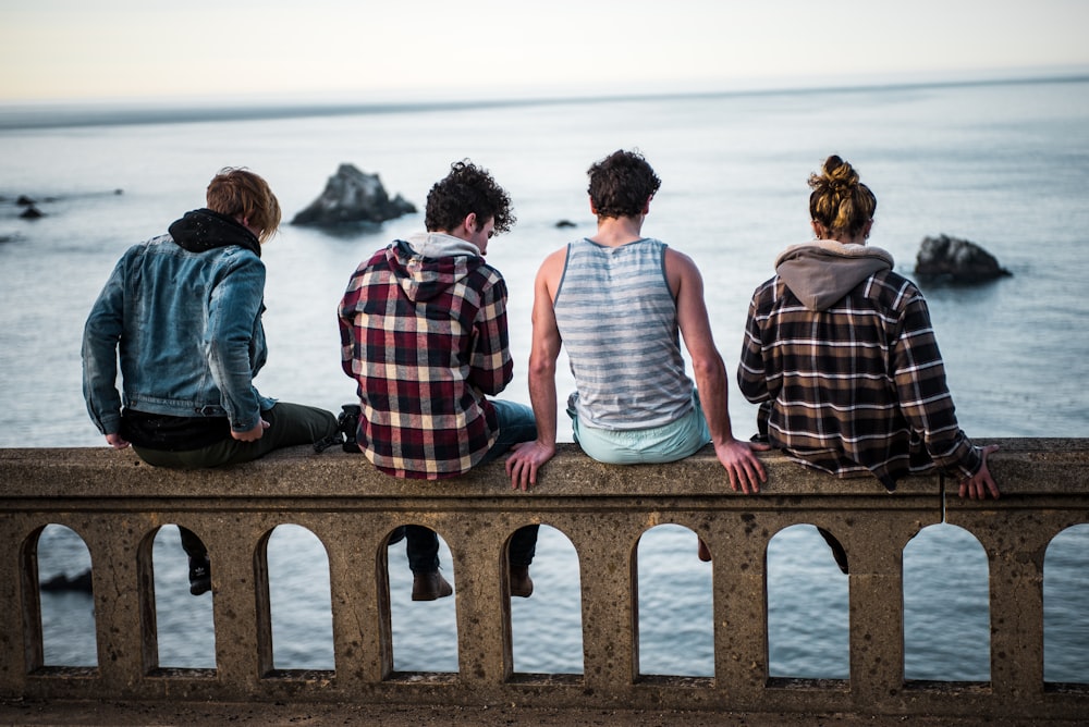 four person sitting on bench in front of body of water