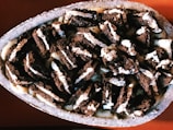 A close-up view of a dessert featuring broken pieces of chocolate cookies mixed with cream, displayed in a stone bowl. The cookies are crumbled into small chunks and are enveloped in a creamy, light-colored sauce, creating a layered texture.