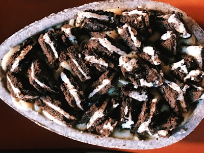 A close-up view of a dessert featuring broken pieces of chocolate cookies mixed with cream, displayed in a stone bowl. The cookies are crumbled into small chunks and are enveloped in a creamy, light-colored sauce, creating a layered texture.