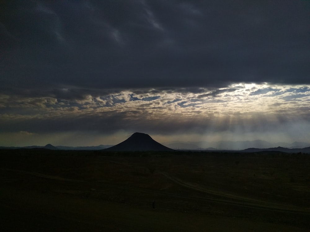 bird's eye view of mountain under cloudy sky with crepuscular rays