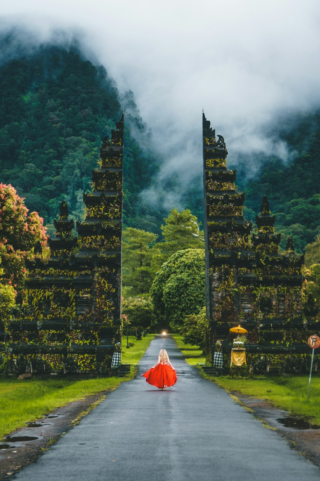 woman wearing red dress running toward gate overlooking foggy mountain during daytime