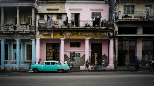 Green classic sedan parked beside a pink two-storey house in Cuba