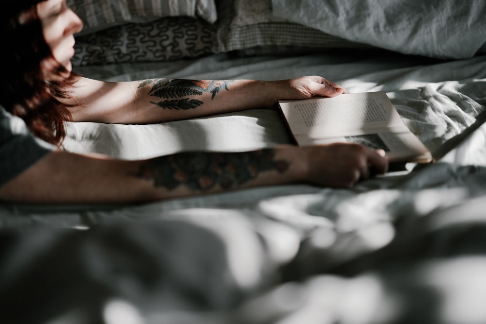 woman holding book while lying on bed