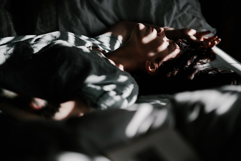 Personne endormie paisiblement dans un lit baigné de lumière tamisée et d'ombres douces, illustrant un sommeil réparateur