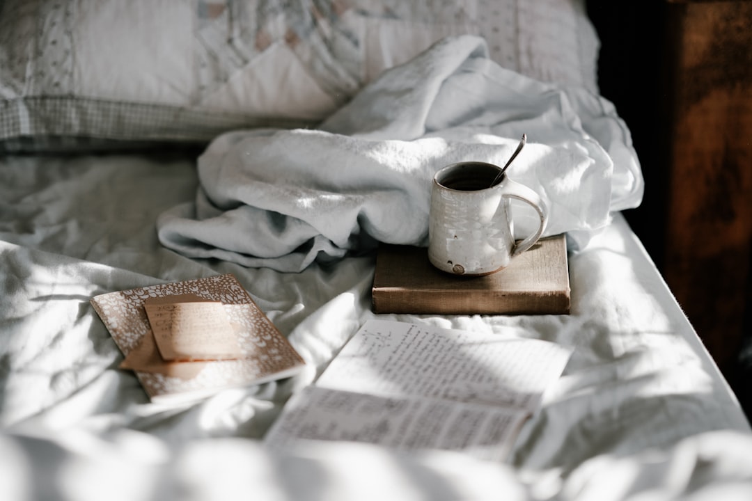 white and gray bed sheet, Mug and notebooks on bed