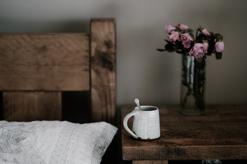 A cozy bedside table with a glowing night lamp, a jar of rich night cream, and a delicate rose beside it.