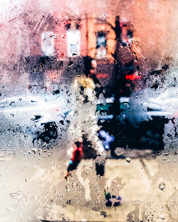 photo of moistened glass with view of person walking on pathway