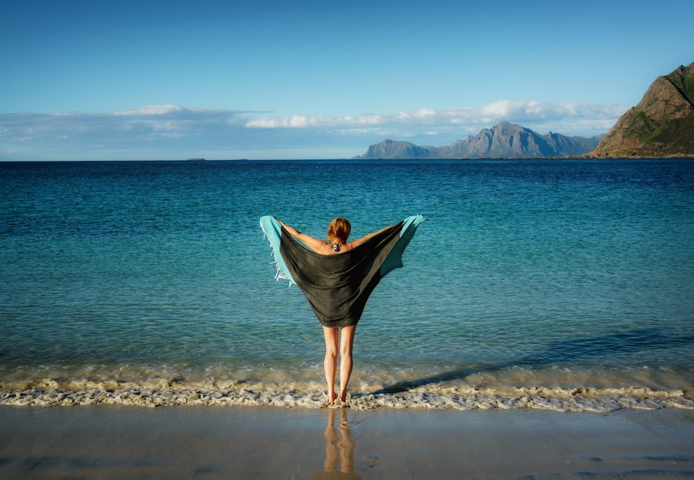 Mulher segurando a toalha preta em pé na praia