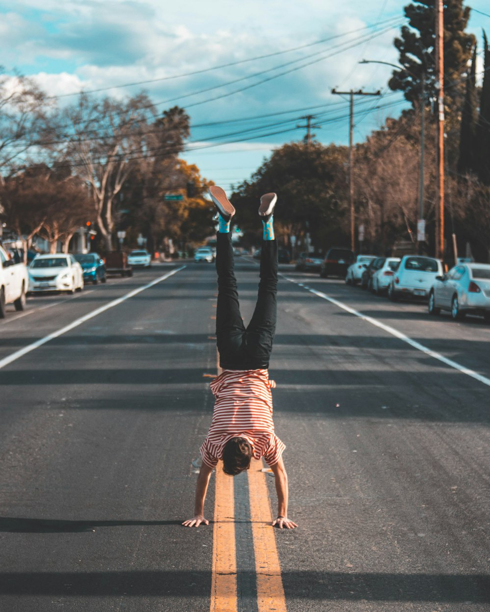 man doing hands stand on asphalt road between trees