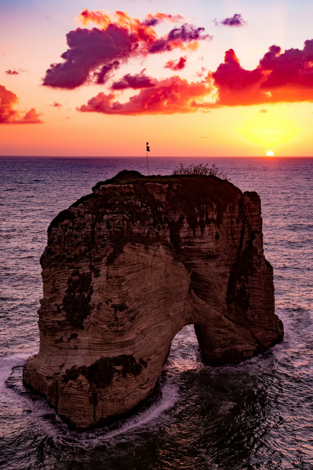 flag on top of rock formation in the middle of sea